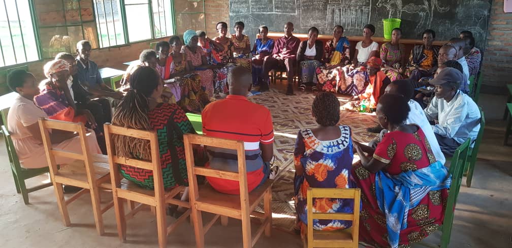 A self-help group of 25+ people come together for a group counselling session; they are all sitting on chairs in a circle. The photo is taken by our local partner (SURF) in Rwanda.