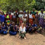 Judy sits on the ground surrounded by self-help group members dressed in brightly coloured clothes